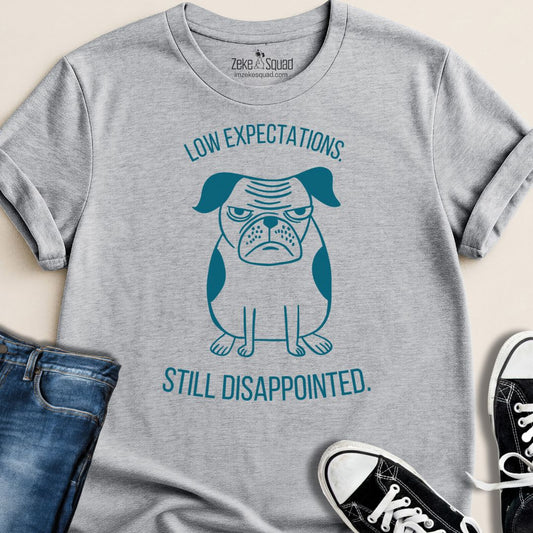 Gray t-shirt with a graphic of a dog and text 'Low expectations still disappointed' on a beige background.