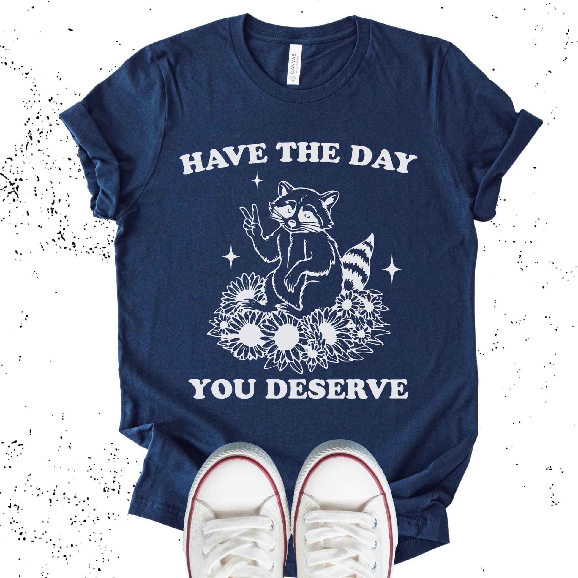 Unisex Zeke Squad T-shirt with the sarcastic phrase “Have the Day You Deserve” and a funny raccoon graphic.