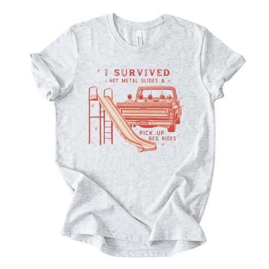 White t-shirt with red graphic and text on a white background that has a pickup truck with children from the 80s riding in the back of the truck and a metal slide.