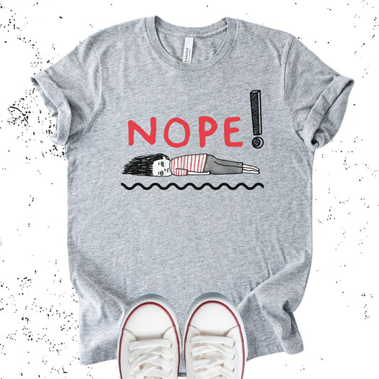 Unisex Zeke Squad T-shirt with the phrase “Nope” and a graphic of a woman lying flat, representing burnout and exhaustion.